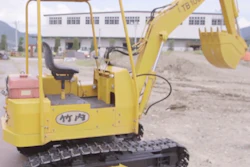 Yellow mini excavator with canopy on construction site with buildings in background