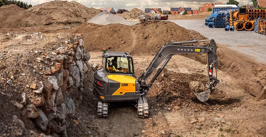 Yellow Volvo excavator digging in rocky construction site with dirt piles