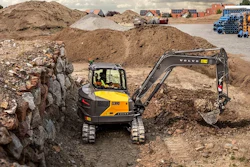 Yellow Volvo excavator digging in rocky construction site with dirt piles