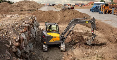 Yellow Volvo excavator digging in rocky construction site with dirt piles