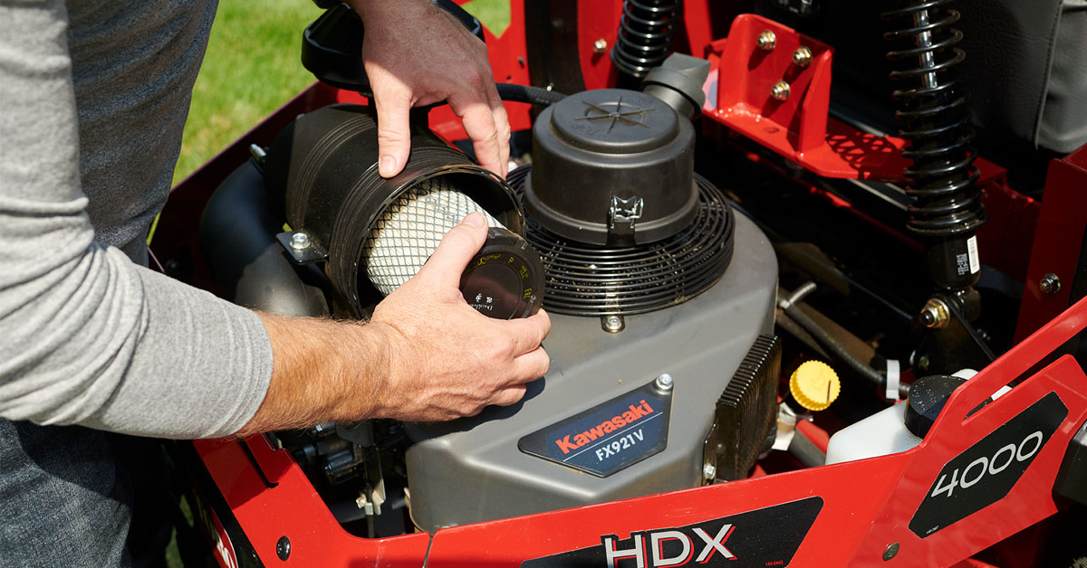 Technician demonstrating red Kawasaki HDX power equipment with air filter removal during maintenance