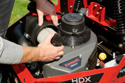 Technician demonstrating red Kawasaki HDX power equipment with air filter removal during maintenance