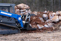 Blue skid steer loader with rock grapple attachment sorting large boulders at construction site