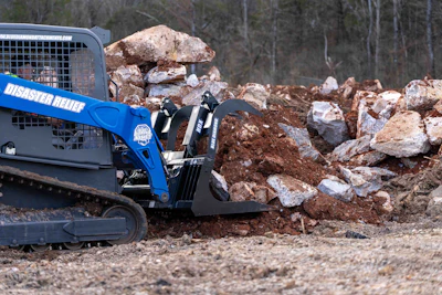 Blue skid steer loader with rock grapple attachment sorting large boulders at construction site