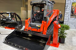 Kubota orange compact track loader with bucket attachment displayed in industrial showroom with landscaping equipment