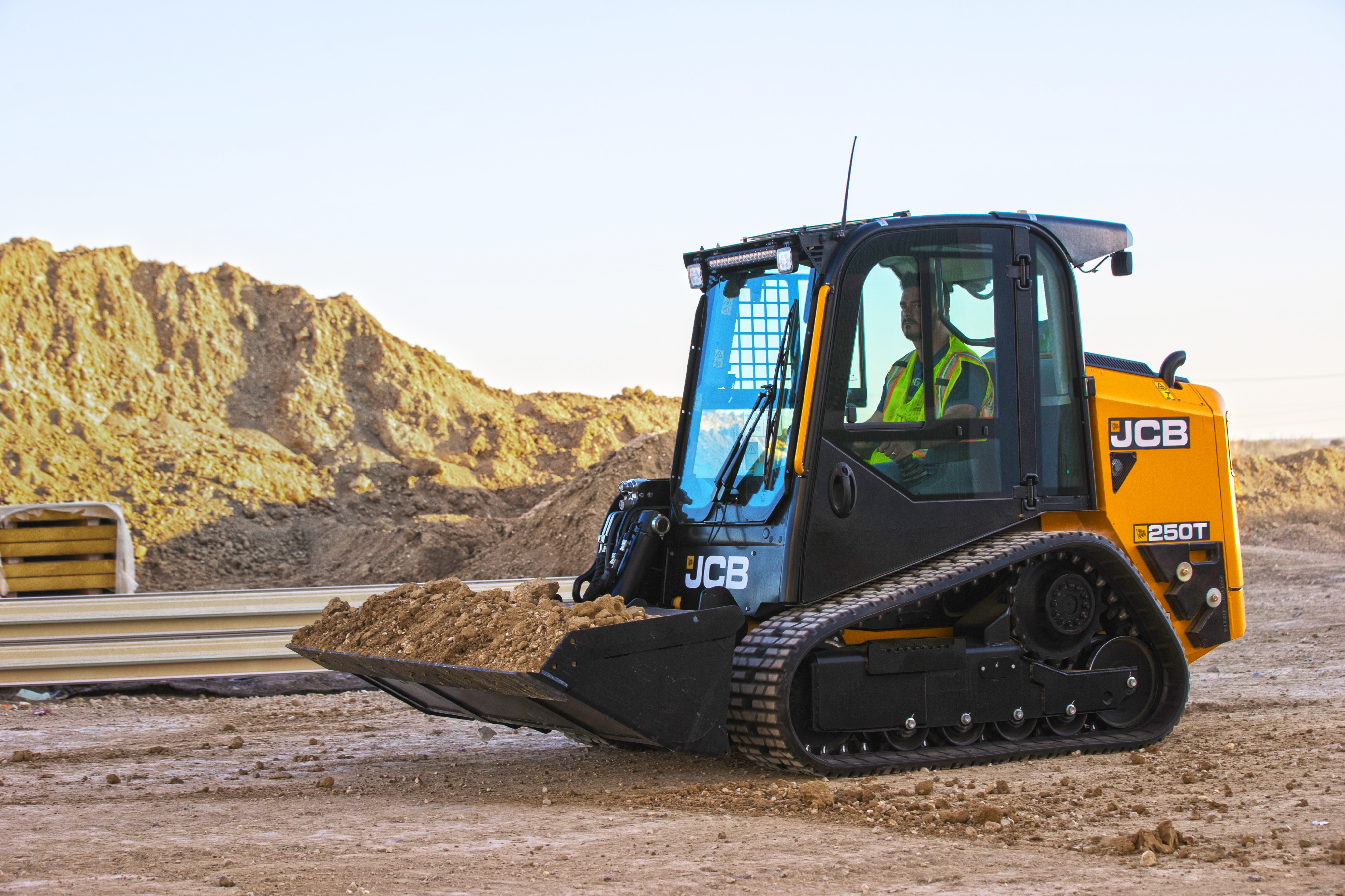 JCB 250T compact tracked loader with operator in quarry setting surrounded by aggregate piles