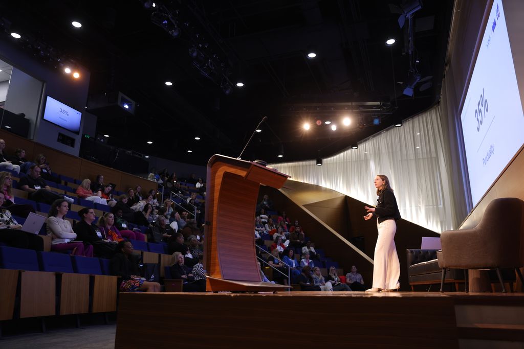 Speaker presenting at conference podium with audience seated in auditorium