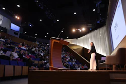 Speaker presenting at conference podium with audience seated in auditorium