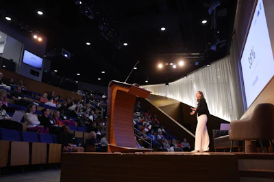 Speaker presenting at conference podium with audience seated in auditorium