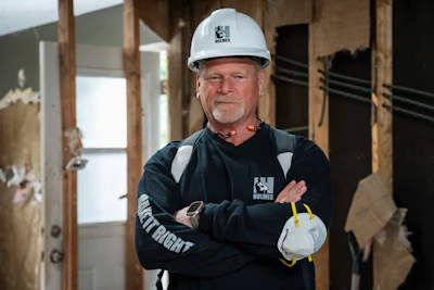 Construction worker in white hard hat and navy Holmes work jacket standing in unfinished building interior