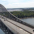 Aerial view of large arch bridge spanning river with forested banks and industrial area in distance