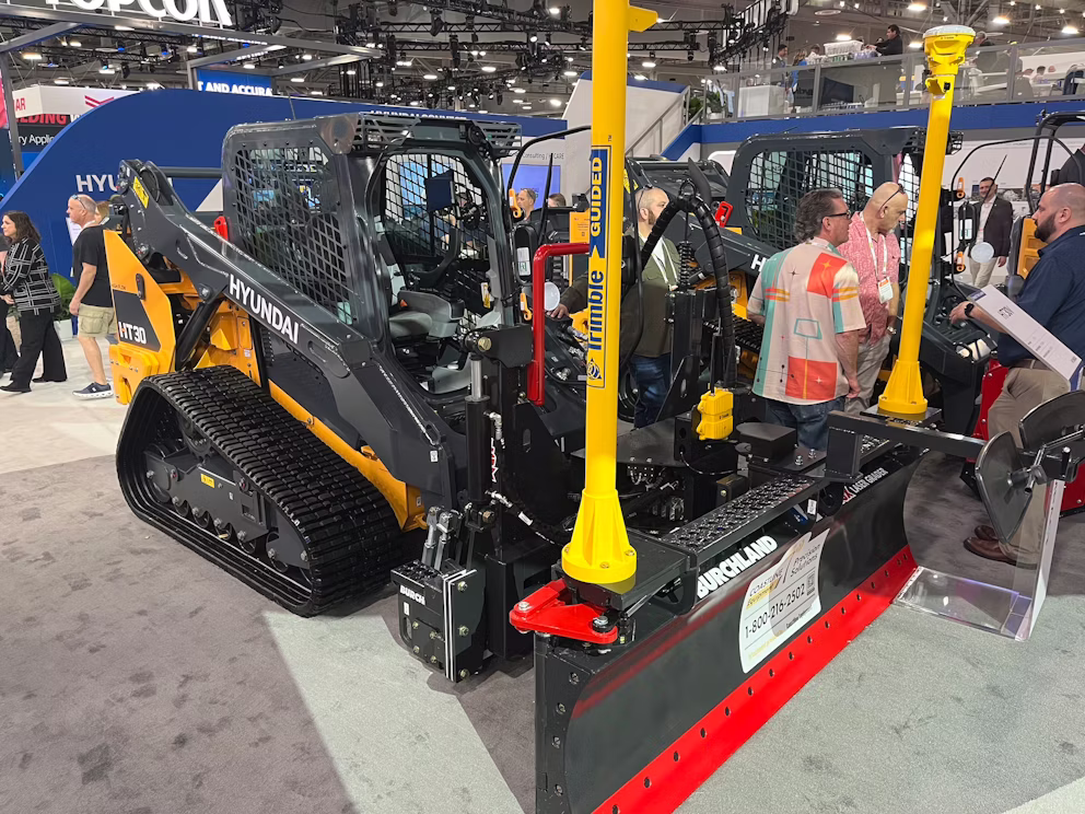 Hyundai heavy equipment display at trade show featuring yellow and black skid steer loader with red snow plow attachment