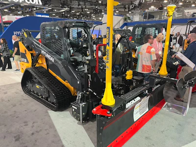 Hyundai heavy equipment display at trade show featuring yellow and black skid steer loader with red snow plow attachment