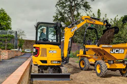 Yellow JCB mini excavator and dumper truck on a construction site with brick wall and landscaping