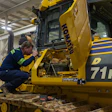 Technician performing maintenance on yellow Komatsu 71PXi excavator in industrial warehouse