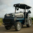 Vintage-style tractor with canopy parked in a vineyard with green grapevines and fence posts