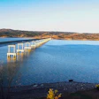 Long causeway with white pillars extending across blue water toward moorland hills under clear sky