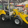 Yellow and white Wacker Neuson wheel loader with landscaping attachment displayed at industrial trade show