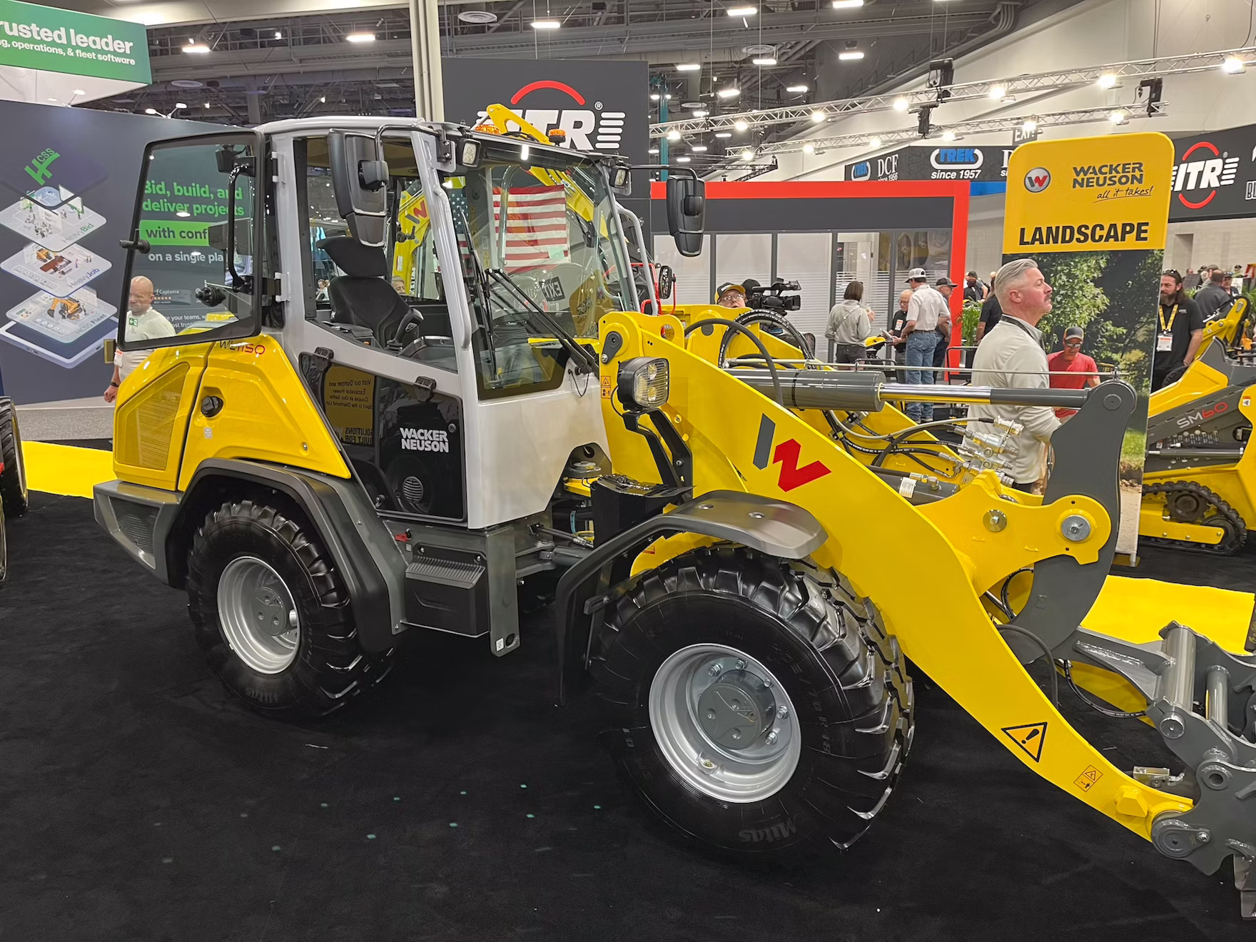 Yellow Wacker Neuson wheel loader with red bucket attachment displayed at indoor trade show booth