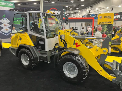 Yellow Wacker Neuson wheel loader with red bucket attachment displayed at indoor trade show booth