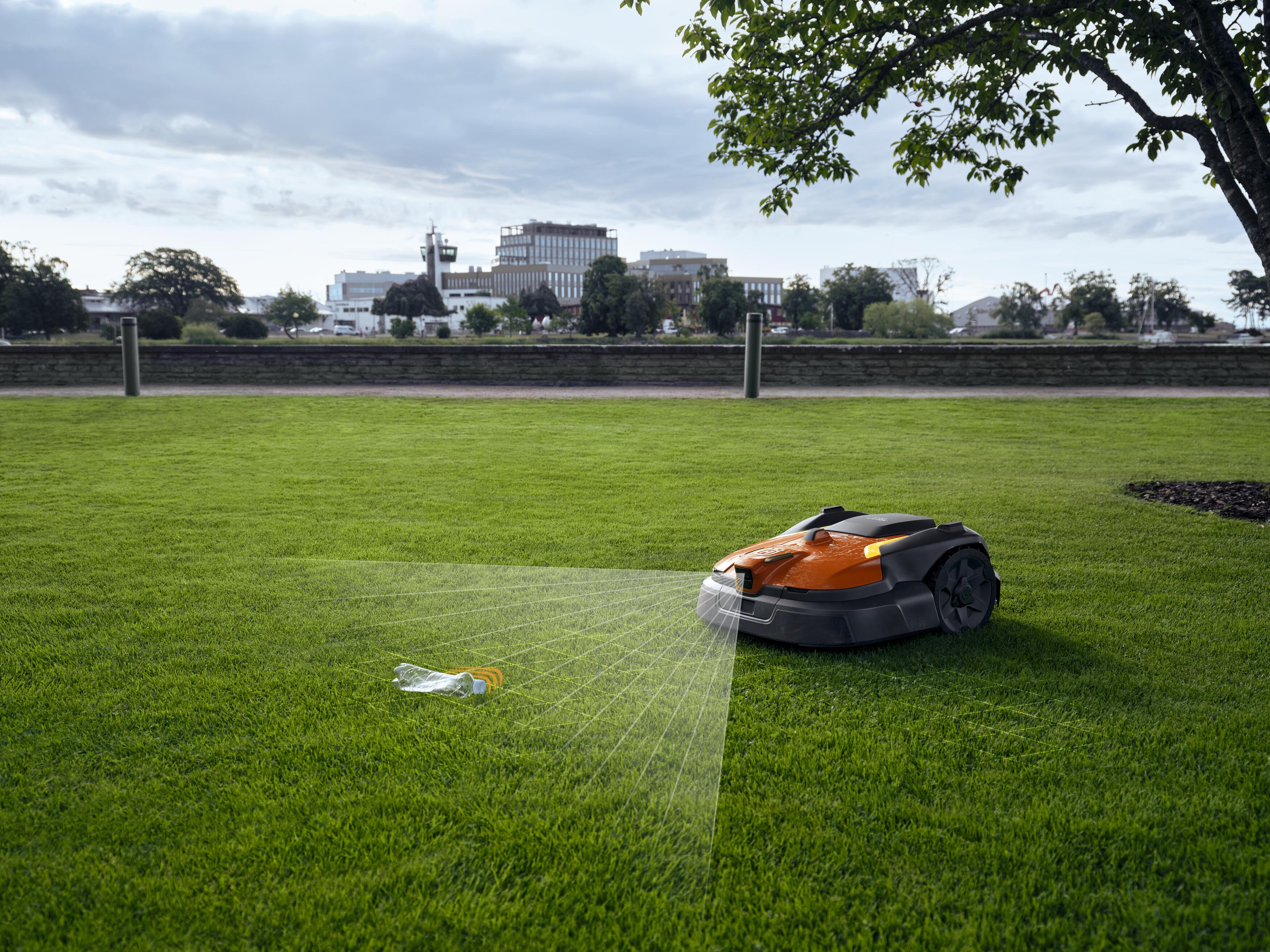 Robotic lawn mower operating on a grass field with urban buildings visible along the horizon
