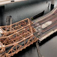Aerial view of industrial waterfront construction site with steel lattice structure, railroad tracks, and highway bridge