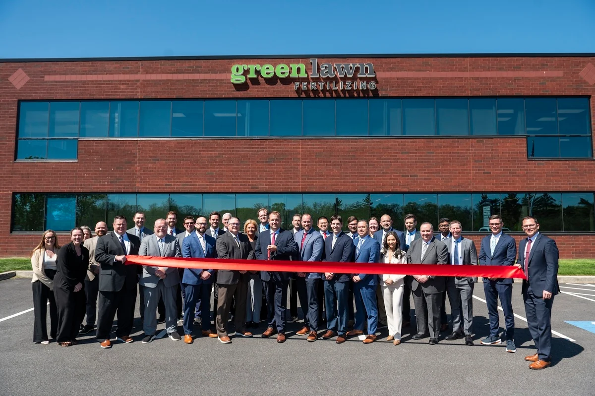 Group of business professionals at Greenlawn ribbon-cutting ceremony in front of brick building