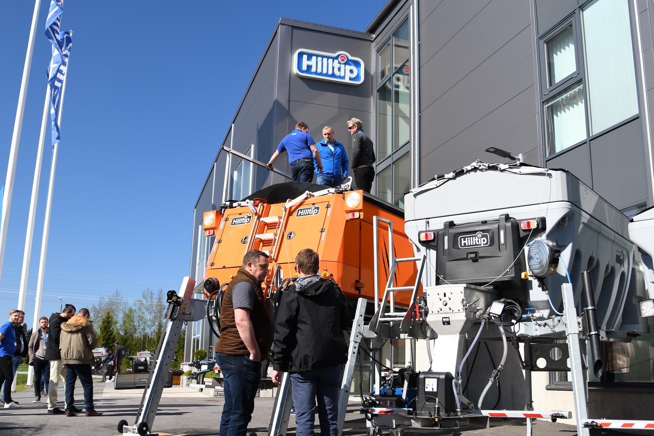 Hilite company facility event with visitors examining orange and white waste management equipment during outdoor demonstration.