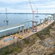 Aerial view of bridge construction site with cranes, concrete pylons, and equipment along waterway