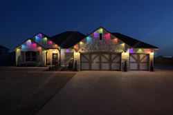 Modern stone house illuminated with colorful RGB lights at dusk, featuring three-car garage and manicured driveway
