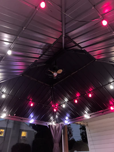 Modern patio pergola with pink and white LED lights and ceiling fan at dusk