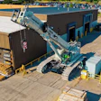 Aerial view of industrial facility with blue mobile crane, metal buildings, and heavy equipment at a commercial work site