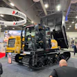 Yellow and black Marooka tracked carrier with open cab on display at industrial trade show with visitors and exhibition booths