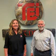 Two professionals posing together in front of KDI company logo and signage