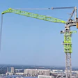 Bright lime-green tower crane with extended jib arm overlooking a sprawling urban cityscape under clear blue sky