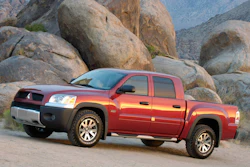 Red pickup truck parked against large granite boulders in a desert mountain landscape