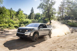 Silver Honda Ridgeline pickup truck driving on dusty dirt road through forest landscape
