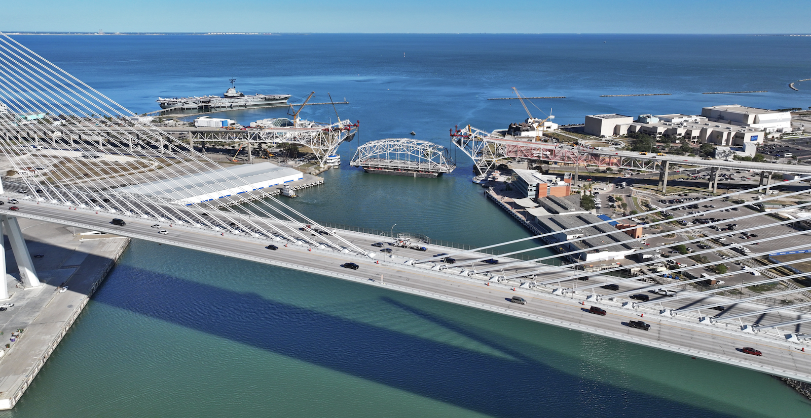 The lowered center span of the original Corpus Christi Bridge rests on a barge as traffic moves across its new replacement structure.