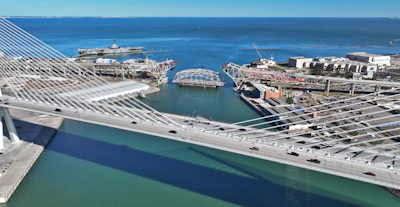 The lowered center span of the original Corpus Christi Bridge rests on a barge as traffic moves across its new replacement structure.