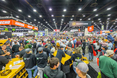 Crowded indoor trade show floor with thousands of visitors browsing equipment displays and branded booths featuring ECHO and Hustler signage.