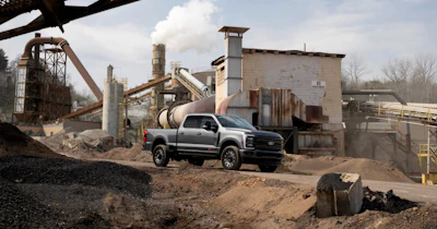 Silver pickup truck parked at industrial aggregate processing facility with conveyor systems and machinery