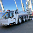 White MAXIM GROVE commercial crane truck parked at construction site with cable-stayed bridge in background
