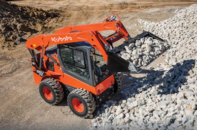 Orange Kubota skid steer loader moving white gravel at a construction site