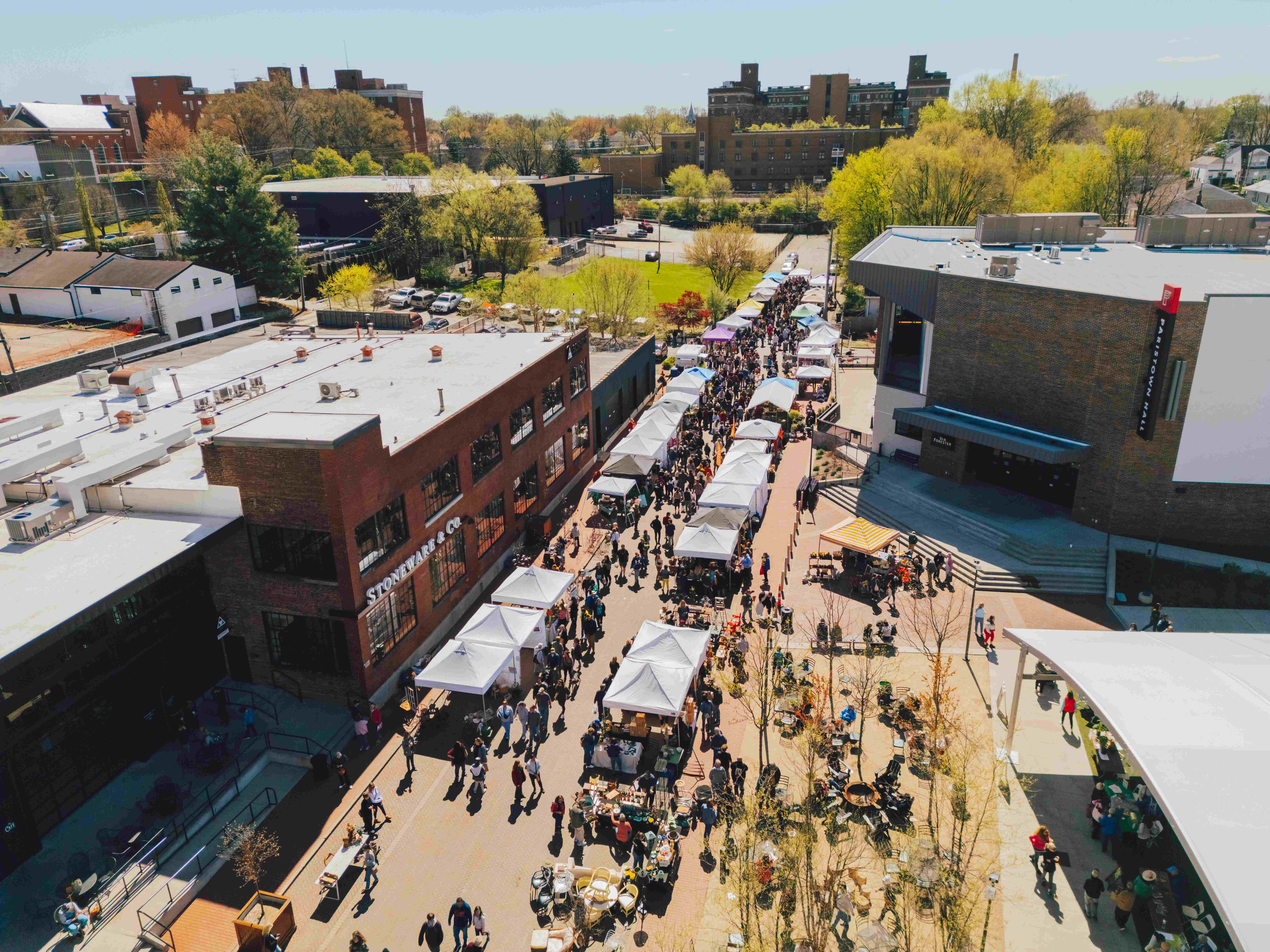 Aerial view of crowded street festival with white vendor tents, crowds, and surrounding urban buildings
