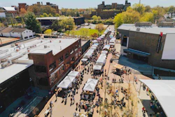 Aerial view of crowded street festival with white vendor tents, crowds, and surrounding urban buildings