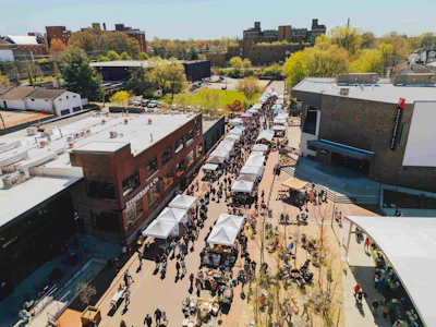 Aerial view of crowded street festival with white vendor tents, crowds, and surrounding urban buildings