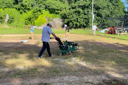 Person operating a green walk-behind aerator machine on a grassy field during outdoor maintenance work