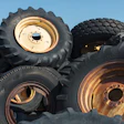Stack of used agricultural tires with tan and rust-colored metal rims against blue sky