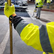 Construction worker in yellow safety vest holding utility pole on job site
