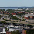 Waterfront cityscape with brick buildings, elevated highway bridge, and river in background under clear sky